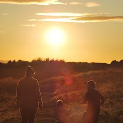 Rear view of mother with sons standing on field against sky during sunset