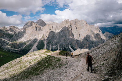 Rear view of man with backpack walking on mountain against cloudy sky