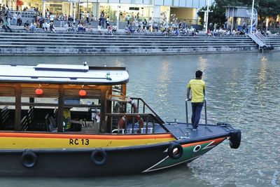 Rear view of man sailing on boat in river at city