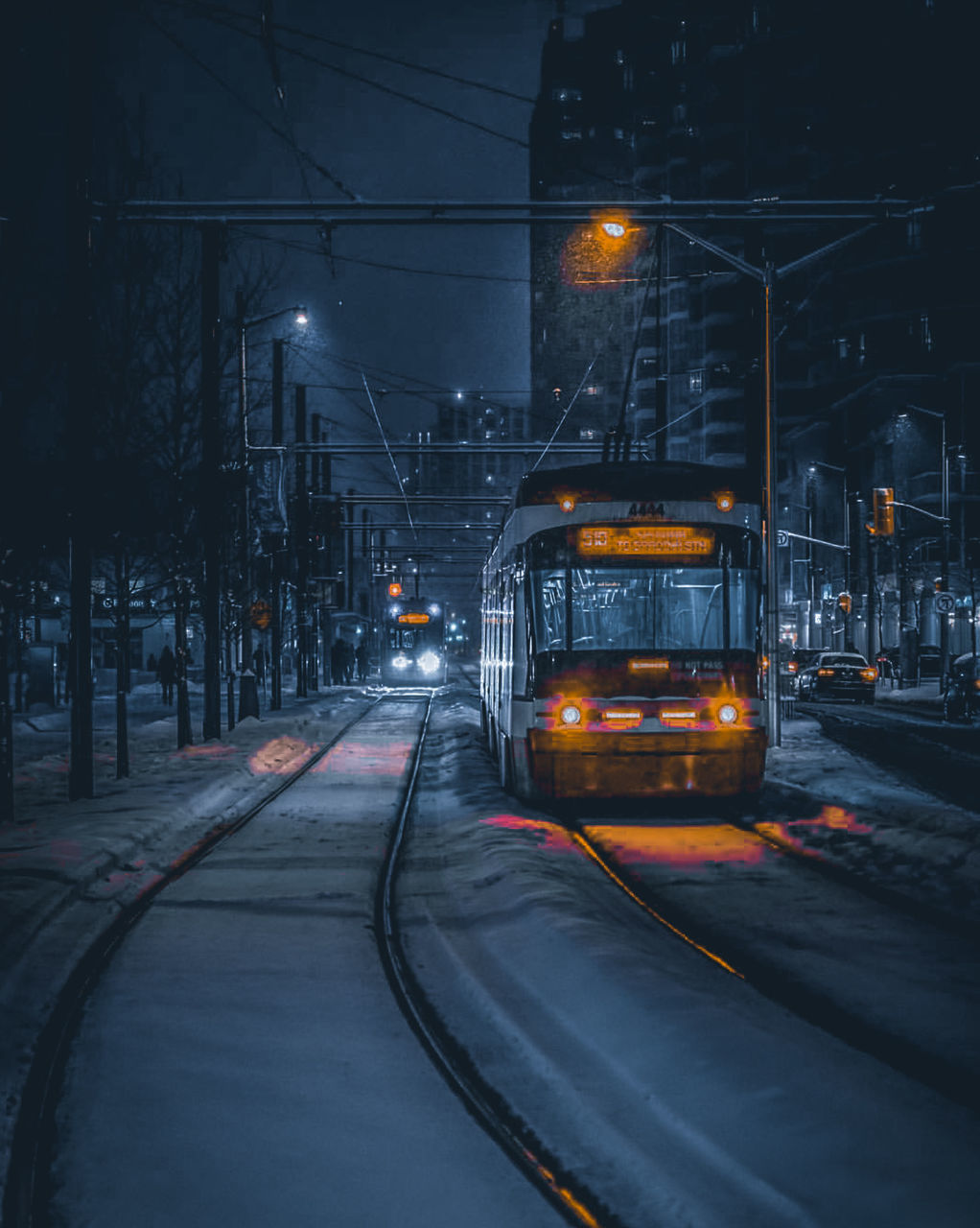 illuminated, transportation, mode of transportation, night, rail transportation, railroad track, track, street, land vehicle, city, architecture, no people, snow, direction, road, cold temperature, cable, the way forward, street light, electricity, snowing