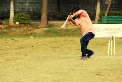Full length of young man playing cricket on field