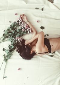 High angle view of sensuous woman with flowers lying on bed