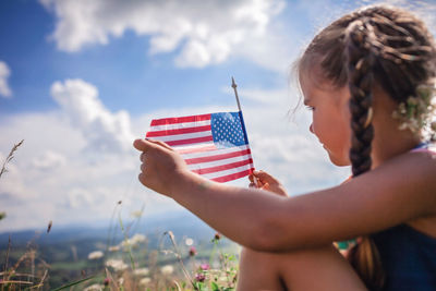 Patriot and national flag day celebration. little patriot sitting on the meadow and holding usa flag