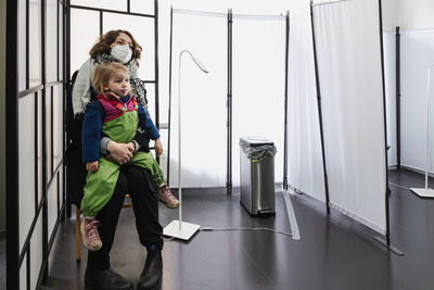 Mother holding child in lap waiting at medical testing facility. full length.