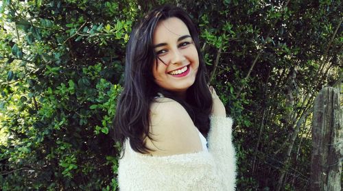 Side view portrait of smiling young woman against plants