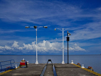 Street lights on pier by sea against sky