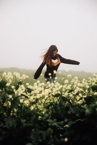 Full length of woman with flowers on field against sky