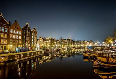 Boats moored on canal amidst illuminated buildings at night