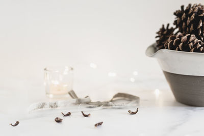 Still life pine cones in stoneware bowl with mini lights, candle