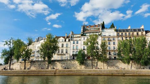 View of buildings by river against cloudy sky