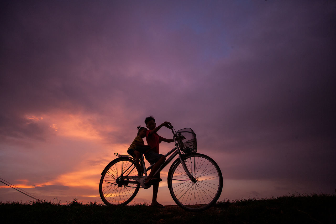 SILHOUETTE BICYCLE ON FIELD AGAINST SKY AT SUNSET