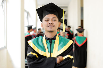 Portrait of woman wearing graduation gown standing against wall