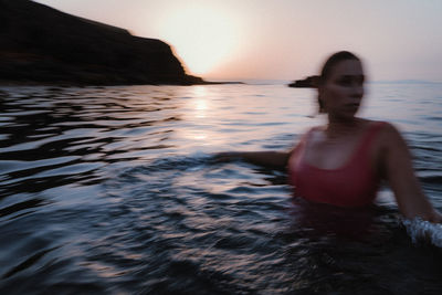 Woman in sea against sky during sunset