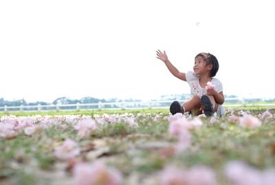 Girl sitting on grass against clear sky