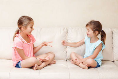 Cute sisters playing while sitting on sofa at home