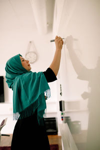 Side view of businesswoman in hijab writing on whiteboard in convention center