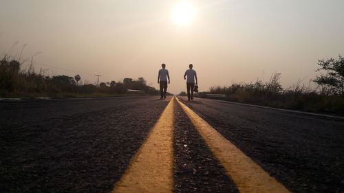 Full length of men walking on country road amidst field against sky