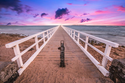 Diminishing perspective of pier over sea against sky during sunset