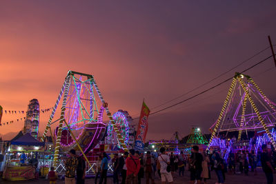 People in amusement park against sky during sunset