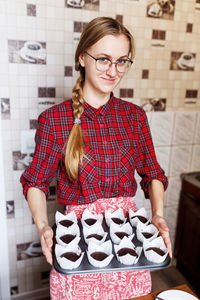 The young woman is holding plate of tasty chocolate cupcakes