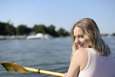 Rear view portrait of young woman smiling while sailing boat in lake