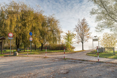 Road sign by trees on field against sky