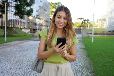 Brazilian woman walking using cell phone texting in city street of curitiba on sunset, parana brazil