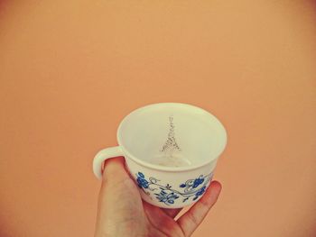 Midsection of woman holding coffee cup against orange background