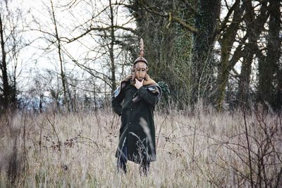 Man with mask standing by bare tree in forest