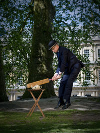 Side view of man striking a teapot with a cricket bat