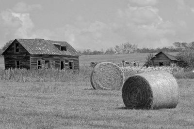 Hay bales on field by house against sky