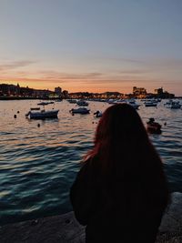 Rear view of woman standing by sea against sky during sunset