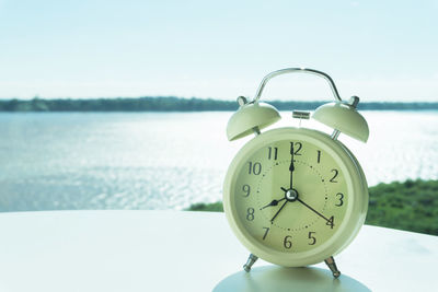 Close-up of alarm clock by sea against sky