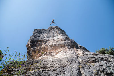 Low angle view of man rock climbing against clear blue sky