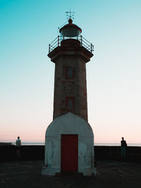 Lighthouse by sea against sky during sunset