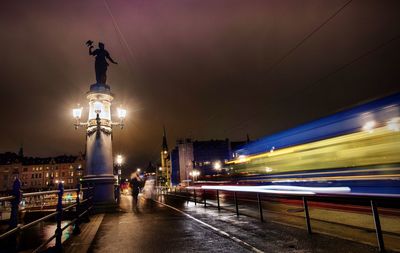 Light trails on illuminated city against sky at night