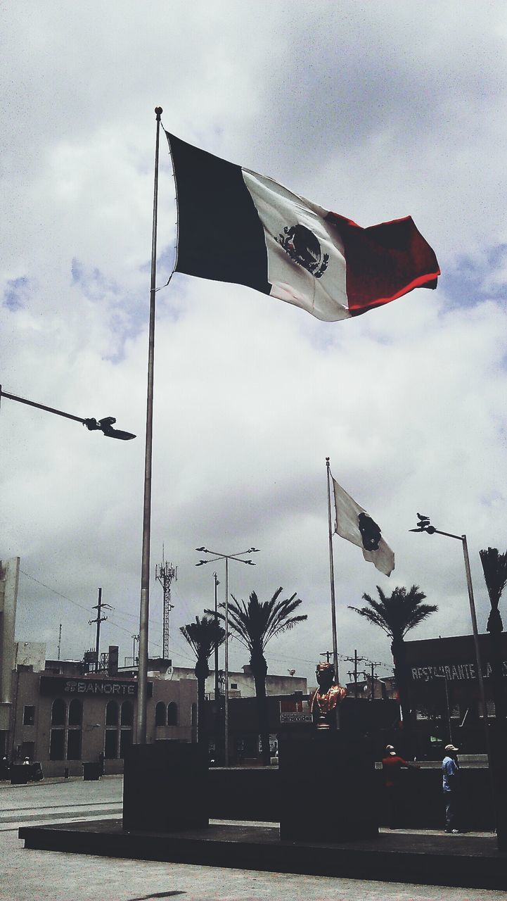 flag, patriotism, identity, national flag, american flag, sky, low angle view, cloud - sky, building exterior, transportation, built structure, architecture, day, cloudy, outdoors, wind, cloud, overcast, culture, pole