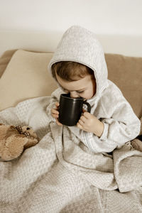 Sick little boy drinking hot tea on the bed at home. unwell, illness child wrapped in a blanket