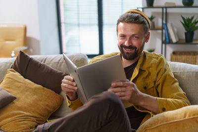 Young man using laptop while sitting on sofa at home