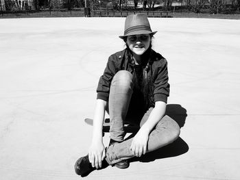 Full length of smiling girl wearing hat sitting on playground during sunny day