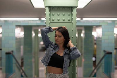 Young woman with hands in hair standing against column