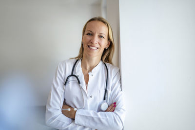 Portrait of smiling female doctor leaning against a wall