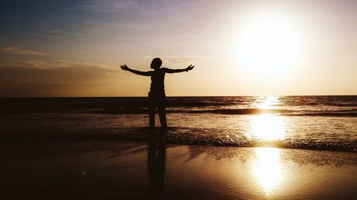 Silhouette man standing with arms outstretched on shore at juhu beach during sunset