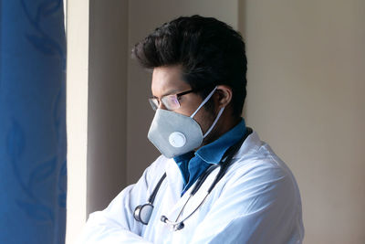 Close-up of doctor wearing mask standing by window