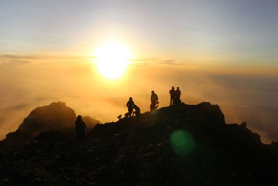 Silhouette people on rock against sky during sunset