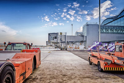 Passenger boarding bridge and vehicles on airport runway against sky