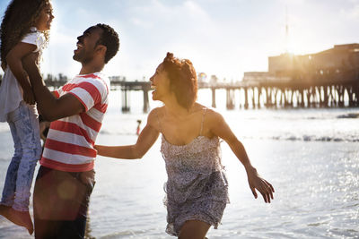 Woman looking at man carrying daughter while enjoying at beach