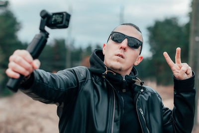 Young man wearing sunglasses filming with video camera
