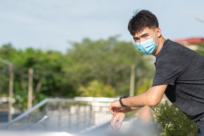 Portrait of young man standing by railing outdoors