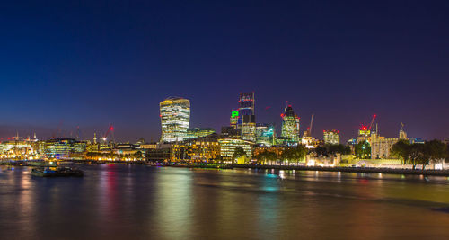 Illuminated buildings by river against sky at night